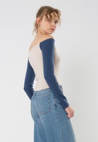 Pitkähihaista puseroa, jossa on nude-väriinen vartalo ja tummansiniset hihat, off-the-shoulder-malli. Yhdistetty vaaleisiin, korkeavyötäröisiin farkkuihin.