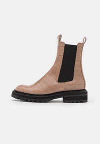 Bottes Chelsea en cuir beige à estampage crocodile avec des panneaux élastiques noirs sur les côtés et une semelle épaisse noire. Comprend des tirants pour un enfilage facile.