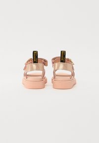 Roza sandali z bleščečimi zlatimi trakovi, nastavljivimi zaponkami za gležnje in teksturiranimi gumijastimi podplati. Črni traki za vlečenje s tekstom "WITH SOLE Bouncing".