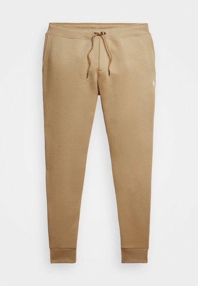 Tan sweatpants made of soft fabric, featuring a drawstring waistband, ribbed cuffs, and a small logo on the lower leg.