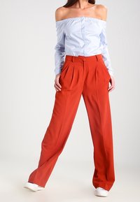 Světle modrá halenka s odhalenými rameny a zapínáním na knoflíky vpředu. Kalhoty s vysokým pasem a širokými nohavicemi v jasně červené barvě s záhyby. Oblečení doplňují bílé tenisky.