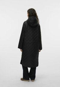 Abrigo largo acolchado negro con capucha, que presenta un patrón de diamantes y abertura lateral para mayor libertad de movimiento. La tela parece suave y con textura.