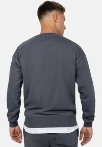 Grijze sweatshirt van textiel met een gestructureerde stof, met lange mouwen en een ronde hals, zichtbare geribbelde manchetten en zoom, gelaagd met een witte shirt eronder.