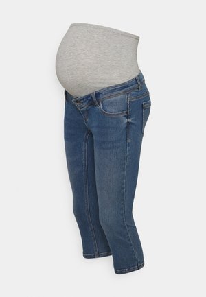Graviditetsjeans med blå denimben og en blød grå elastisk linning, der dækker en gravid mave, vist mod en hvid baggrund.