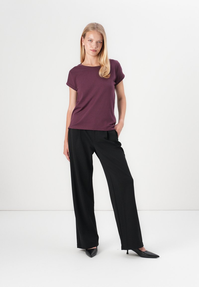 Kurzärmliges, rundhalsiges lila T-Shirt, kombiniert mit schwarzen weit geschnittenen Hosen und spitzen schwarzen High Heels. Glattes Gewebe mit lockerer Passform.