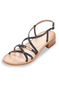 Sandal nera con cinturini, caratterizzata da un basso tacco in legno, una soletta liscia color beige e dettagli incrociati con una leggera finitura testurizzata. Cinturino alla caviglia regolabile.