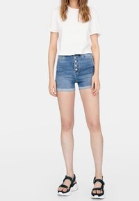 Ljusblå denimshorts med hög midja, femknäppning framtill och uppvikt fåll. Kombinerad med en enkel vit t-shirt och svarta sandaler.