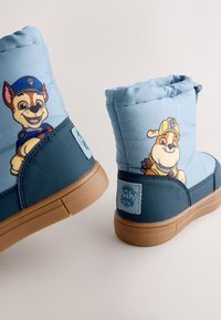 Hellblaue Winterstiefel mit braunen Gummisohlen, verziert mit Cartoon-Hundemotiven. Weicher Stoff, gepolstertes Design und ein seitliches Logo-Patch.