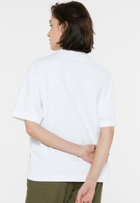 Weißes Baumwoll-T-Shirt mit kurzen Ärmeln und Rundhalsausschnitt. Verfügt über ein Etikett an der linken Seitennaht. Einfaches und minimalistisches Design.