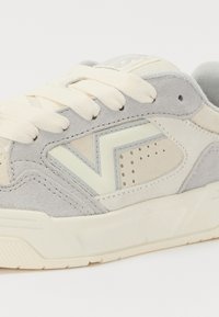 Szürke és krémszínű velúr sneaker, texturált kiegészítőkkel, perforált részletekkel, krémszínű fűzőkkel és világos színű gumitalppal.