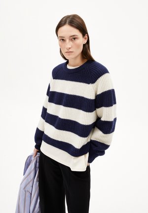Navy and white striped knitted sweater with ribbed texture, round neckline, and long sleeves, worn over a white top and paired with black pants.