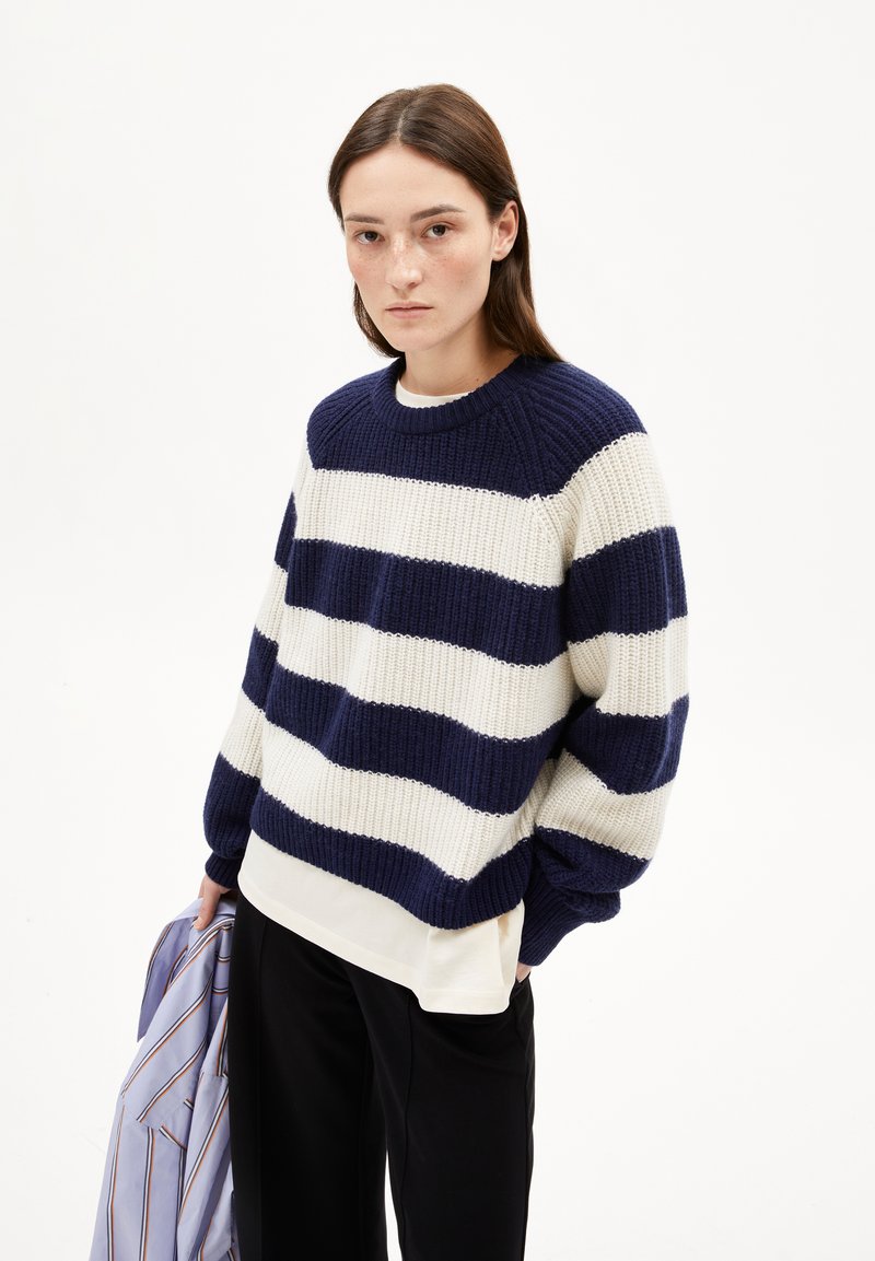 Pull en tricot rayé bleu marine et blanc avec texture côtelée, col rond et manches longues, porté sur un haut blanc et associé à un pantalon noir.