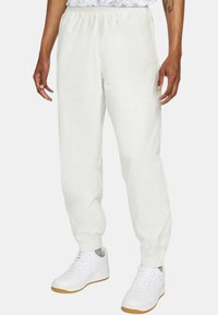 Vita, lätta joggarbyxor med elastisk midja, muddade anklar och en liten Nike-logga på vänster sida.