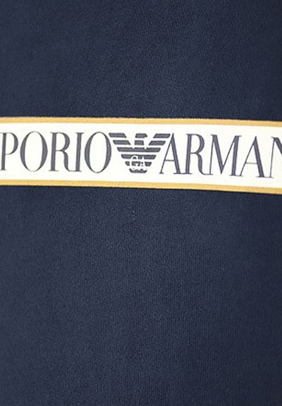 Tessuto blu navy con una texture liscia, caratterizzato da una banda orizzontale bianca e dorata che presenta il logo "EMPORIO ARMANI" con l'emblema dell'aquila.