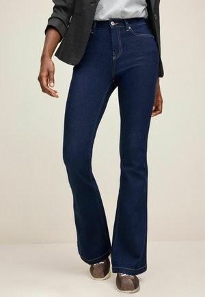 Jeans dzwonowe w ciemnoniebieskim kolorze z widocznymi detalami szwów. Tkanina ma gładką fakturę, dopełnioną klasycznym zapięciem na guzik.