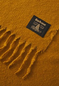 Wool scarf in vibrant mustard yellow, featuring fringe edges and a black label with white lighthouse graphic and brand name "Barbour."