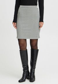 Sorte og hvide houndstooth-mønstrede nederdel sat sammen med en tætsiddende sort langærmet top og knæhøje, blanke sorte støvler.