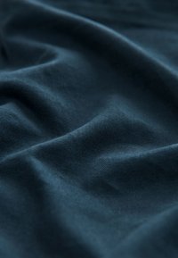 Diepblauwe stof met een gladde textuur, voorzien van subtiele golvingen en plooien. Het materiaal lijkt lichtgewicht en zacht.