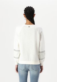 Biely sweatshirt s textúrovaným zadným dielom a pruhovanými rukávovými akcentmi. S okrúhlym výstrihom a rebrovaným lemom, vyrobený z mäkkej tkaniny.