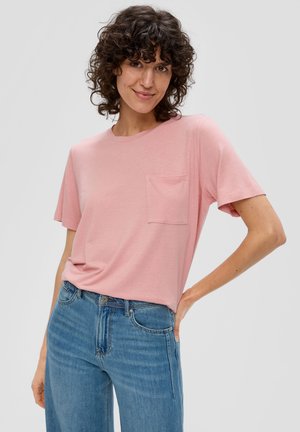 Hellrosa T-Shirt aus weichem Stoff, mit Rundhalsausschnitt und einer einzigen Brusttasche, kombiniert mit blauen Denim-Jeans.