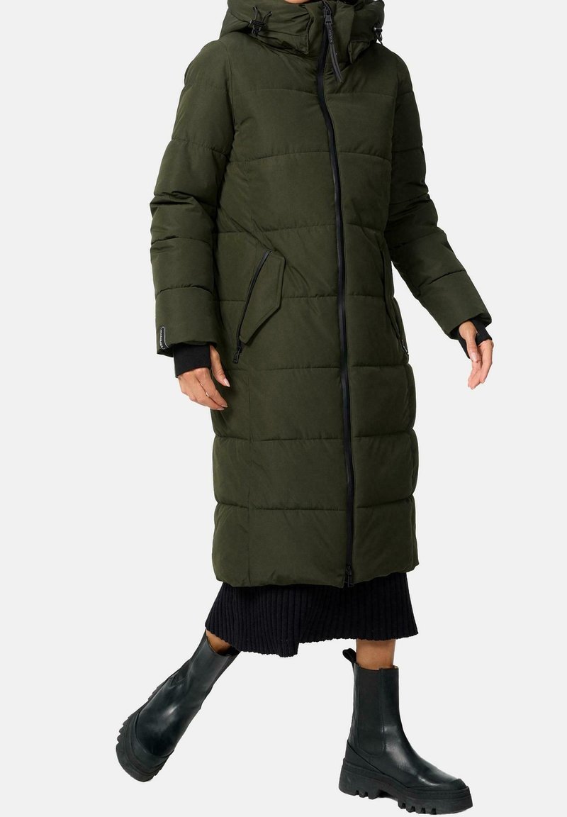 Olivengrøn puffermantel med hætte, udstyret med lynlåslommer, en lynlåslukning foran og et quiltet mønster, kombineret med sorte ankelstøvler.