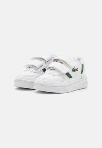 Sneaker bianche con due cinturini in Velcro, accenti verdi, punta perforata, suola in gomma testurizzata e logo ricamato sul lato.