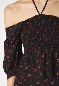 Abito nero floreale con accenti rossi, con maniche scoperte, corpino arricciato e design a strati di volant. Tessuto leggero con texture.