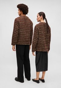 Štruktúrované, viacfarebné pletené bundy v burgundských a zelených tónoch na dvoch postavách, skombinované s čiernymi širokými nohavicami a koženou sukňou.