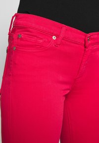 Jeans de cintura alta, ajustados en un vibrante denim rosa con herrajes dorados, bolsillos laterales y detalles de costura a tono.