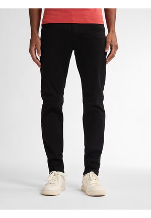Pantalones de mezclilla negros con un ajuste slim, con cinco bolsillos y costuras sutiles. Combinados con zapatillas de color crema.