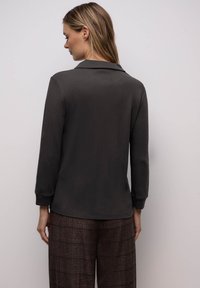 Dunkelgraues Polohemd mit langen Ärmeln und Kragen, mit gerippten Bündchen und lockerer Passform, kombiniert mit strukturierten braunen gemusterten Hosen.