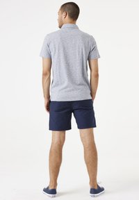 Polo de rayas grises y blancas, de manga corta, combinado con pantalones cortos azul marino y zapatos de lona azules. Tejido suave, diseño de ajuste clásico.