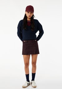 Granatowy sweter z dekoltem w serek, bordowy kamizelka pod spodem, strukturalna bordowa mini spódnica, granatowe skarpetki oraz białe trampki z czarnymi paskami.