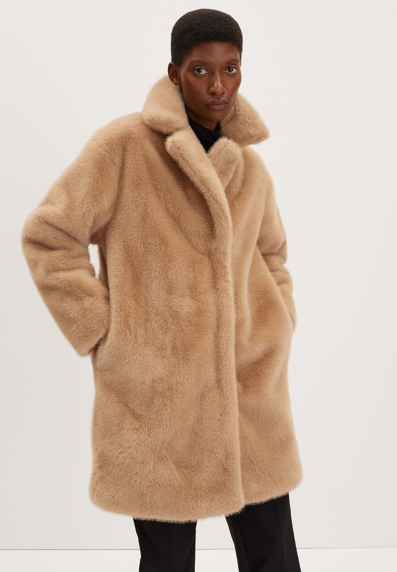 Cappotto in pelliccia sintetica beige con ampio colletto, design oversize e tasche laterali. Texture morbida con un finish liscio. Vestibilità sagomata all'orlo.
