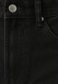Mustan denim-kankaan sileä pinta, jossa on hopeinen nappi ja huomaamattomat tikkausdetailit, sekä tasku oikealla puolella.