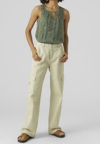 Groen geplooid mouwloos topje met bloemenpatroon, gecombineerd met losse beige cargobroek met zijzakken en een rechte pijp.