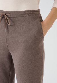 Pantalones de chándal de algodón marrón con cintura ajustable, bolsillos laterales y un acabado texturizado suave. Adecuados para uso casual.
