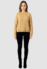 Jersey de punto beige con diseño de trenzas, cuello redondo y puños de canalé. Se lleva con jeans skinny negros y botas de tobillo.