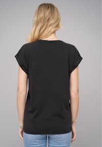 T-shirt en coton noir avec des manches courtes retroussées, un col rond et une coupe décontractée, présenté sur une personne de dos face à l'appareil photo.