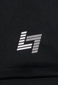 Un tissu noir avec une surface texturée présente un design de logo audacieux en blanc intégrant des rayures et des grilles.