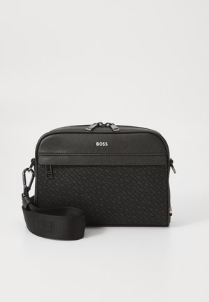 Borsa a spalla nera in materiale texturizzato, dotata di chiusura con zip, logo sul davanti e tracolla rimovibile. Forma rettangolare compatta.