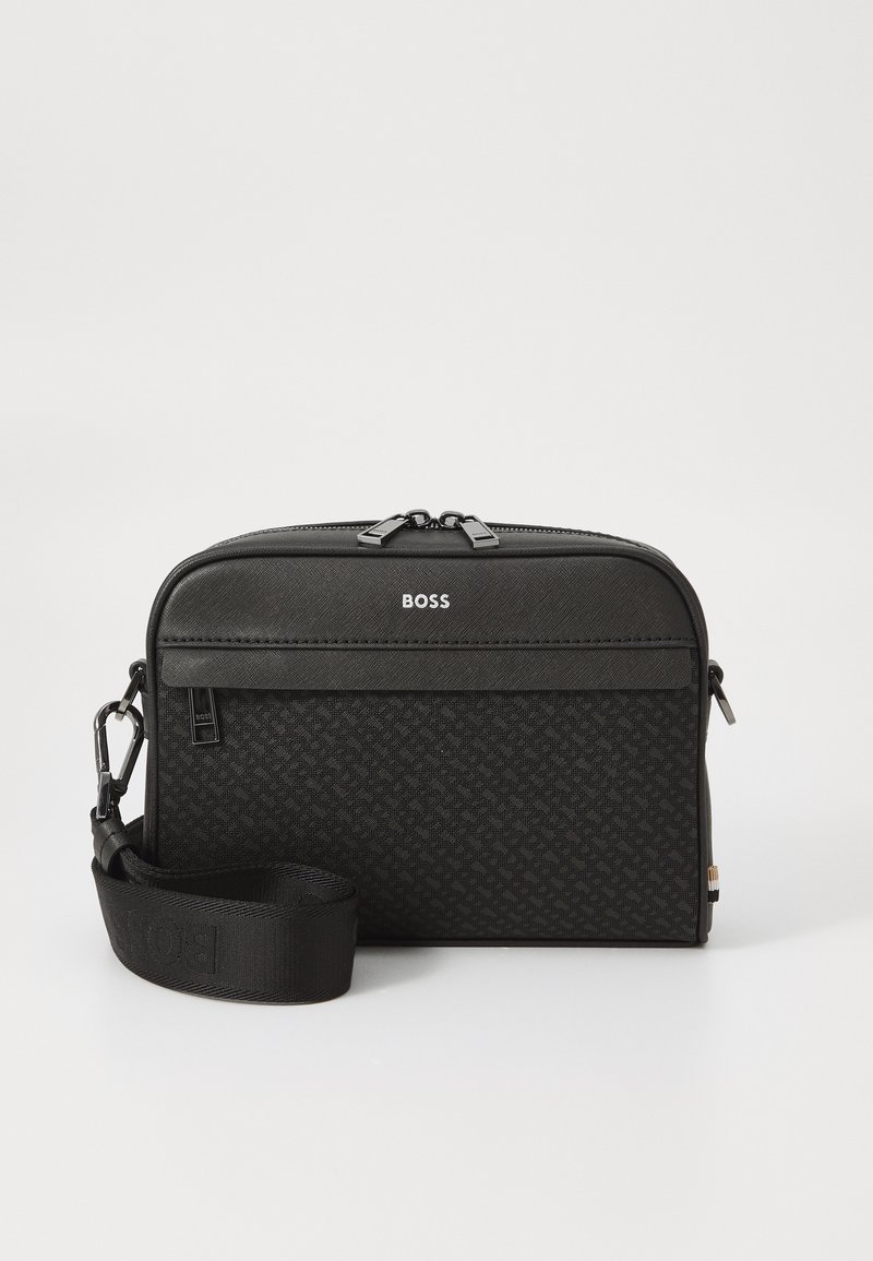 Borsa a spalla nera in materiale texturizzato, dotata di chiusura con zip, logo sul davanti e tracolla rimovibile. Forma rettangolare compatta.