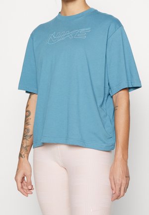 Personne portant un t-shirt Nike bleu ample et des leggings rose clair avec des tatouages visibles sur les deux bras.