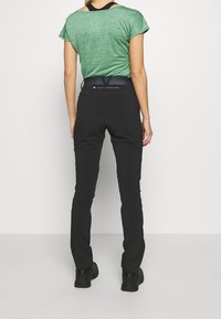 Zelený krátký rukávový top v kombinaci s přiléhavými černými kalhotami s pružným pasem a zipovou kapsou vzadu. Černá obuv dotváří outfit.