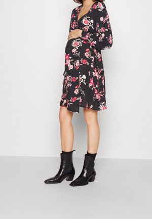 Robe noire à fleurs avec manches longues et col en V, ornée de fleurs roses et blanches. Associée à des bottines noires à talon carré.