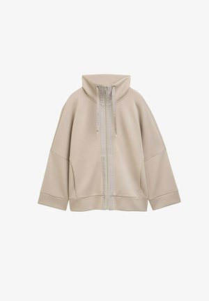 Beige ritsjack met hoge kraag, trekkoorden, verlaagde schouders en brede manchetten, ontworpen voor casual draag.
