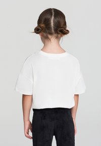 Biała koszulka z krótkim rękawem o luźnym kroju, z okrągłym dekoltem, w połączeniu z czarnymi spodniami sztruksowymi, widok z tyłu.