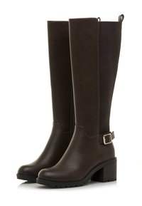 Botas marrones hasta la rodilla hechas de cuero, con paneles laterales elásticos, acento de hebilla y suela de goma texturizada. Diseño de tacón cuadrado.