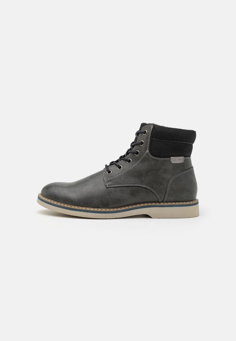 Bottine en cuir gris foncé avec col rembourré noir, lacets à l’avant, semelle beige et couture visible sur fond blanc.