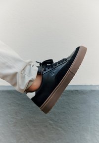 Sneaker in pelle nera e suede con suola in gomma marrone, design con lacci e dettagli di accentuazione sul tallone. Presenta una superficie testurizzata.